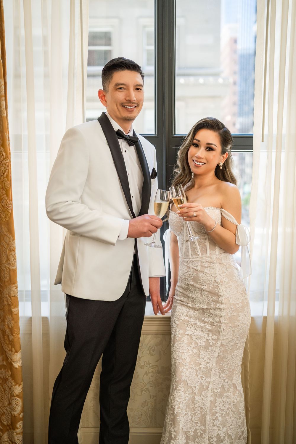 A couple shares a joyful moment together in formal wedding attire near bright windows.