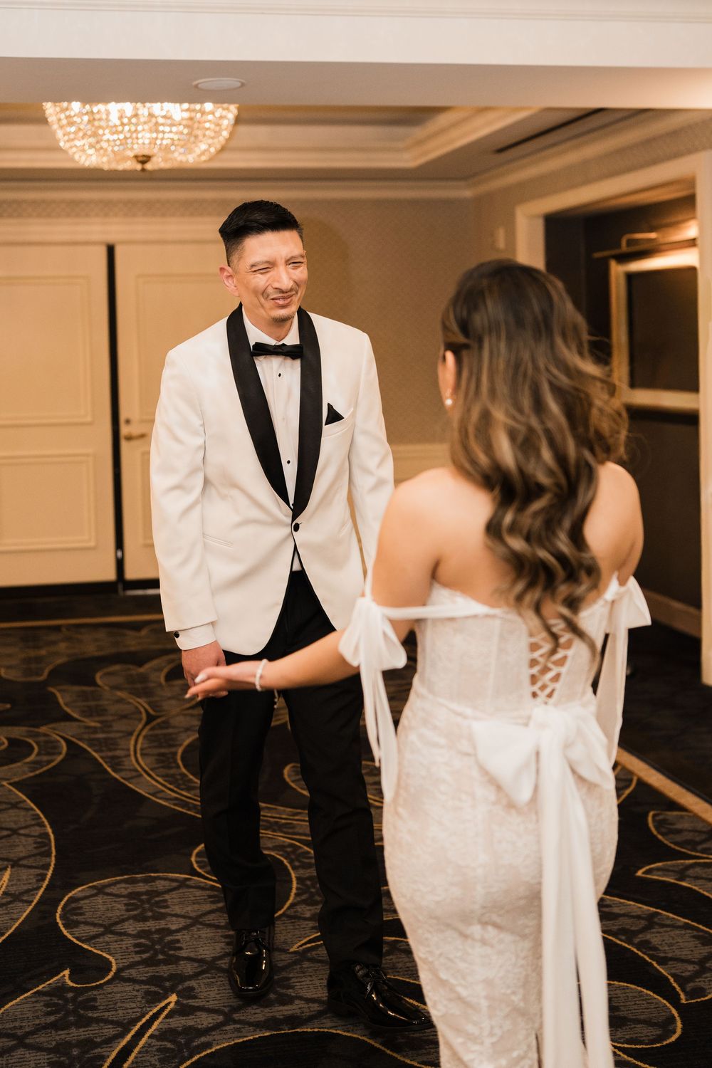 A couple shares a joyful moment in formal attire at an elegant ballroom reception with crystal chandeliers.