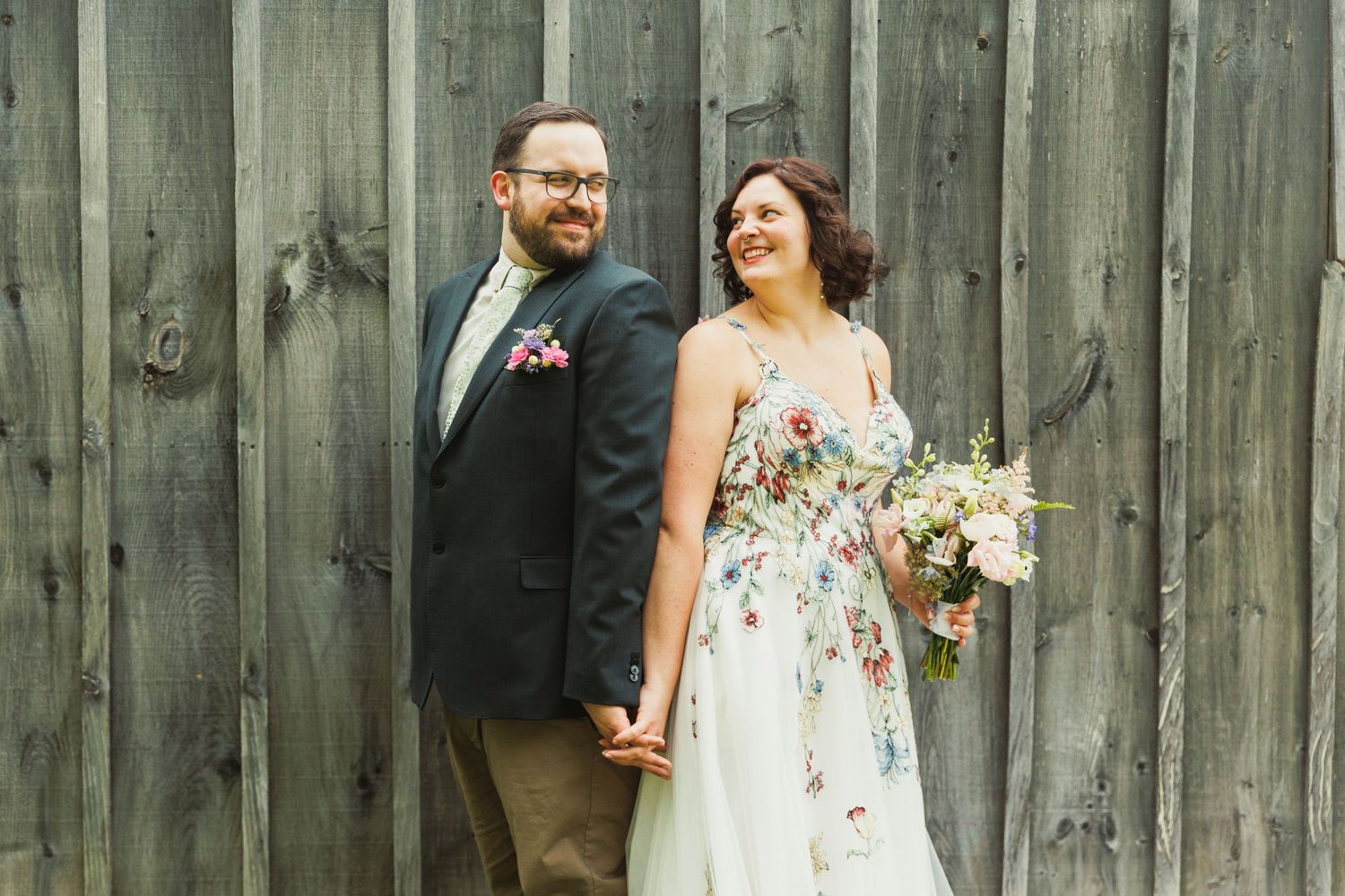 Wedding couple shares intimate moment against weathered wooden barn wall background.