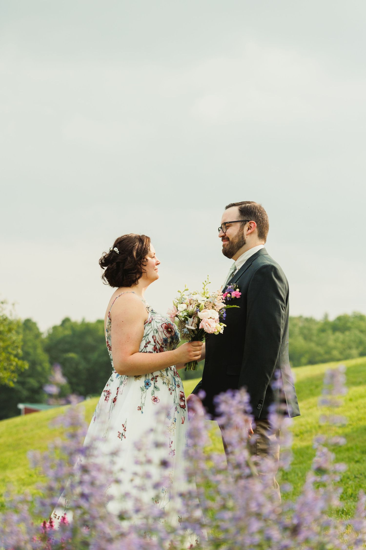 A couple poses together in a field of purple wildflowers during a romantic outdoor photoshoot.