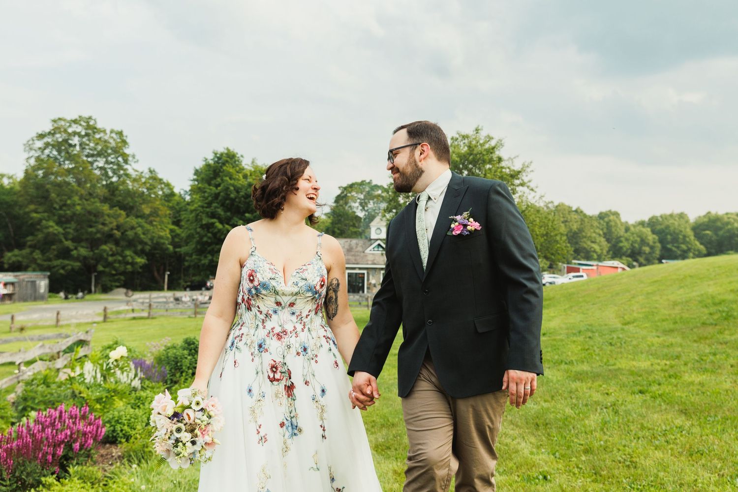 A couple walks hand in hand through a sunny field during their wedding day photoshoot.