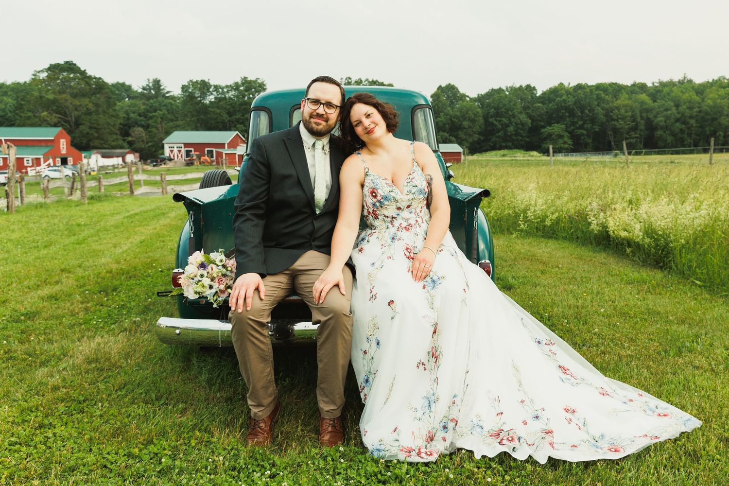 Newlyweds sit together on the tailgate of a classic teal pickup truck during their wedding photos.