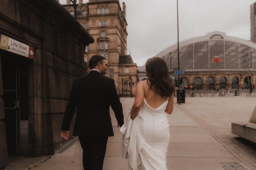 Couple walking together on a city bridge during sunset with urban architecture in the background.