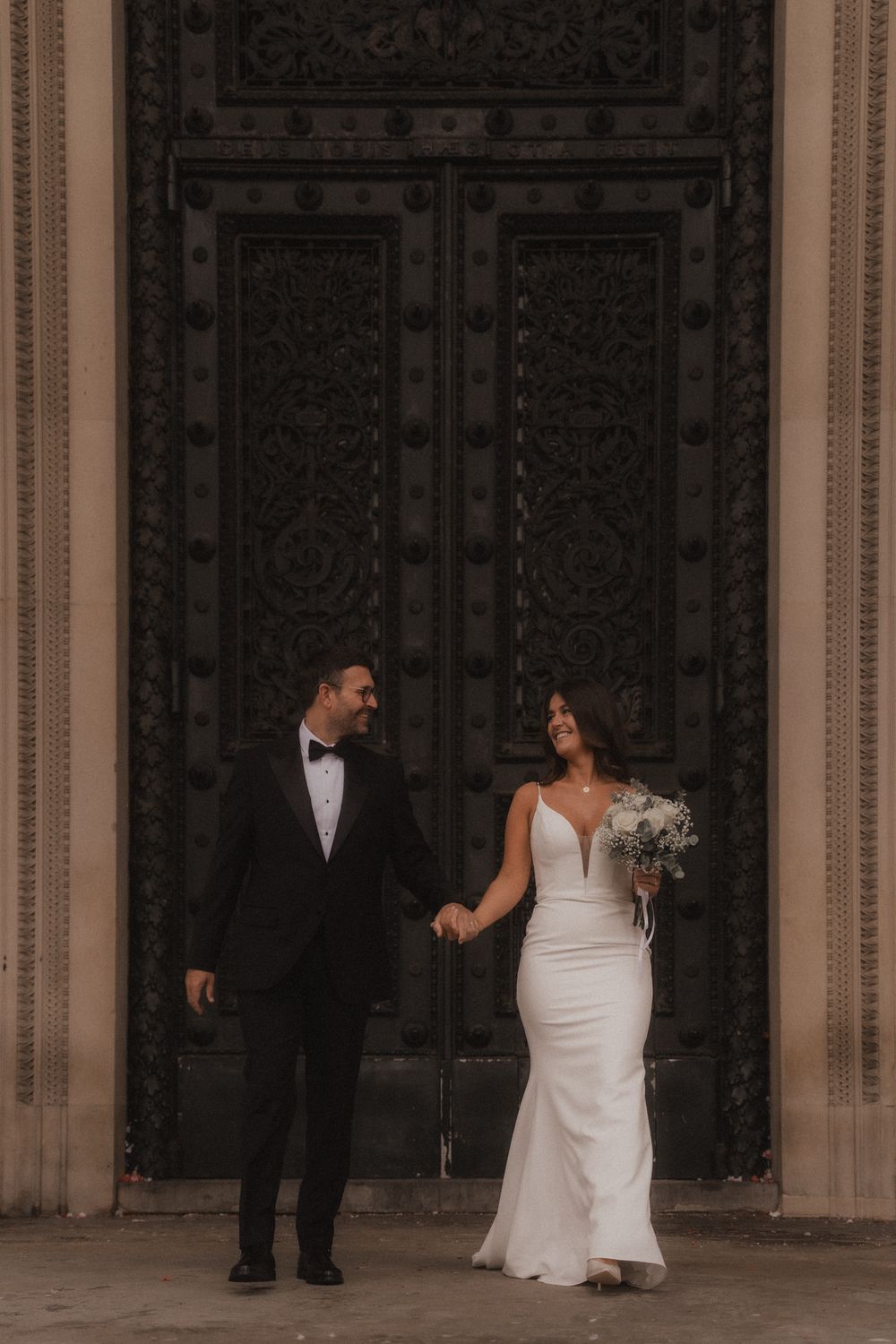 Wedding group stands before decorative black doors in a formal architectural setting.