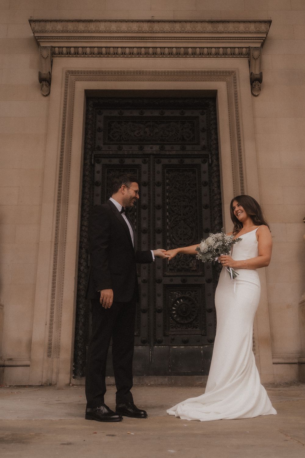 A couple in wedding attire stands before an ornate vintage door during their romantic outdoor ceremony.