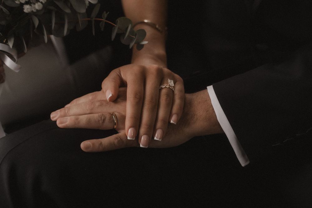 Close-up shot of hands with wedding rings exchanging vows during an intimate ceremony in dark lighting.