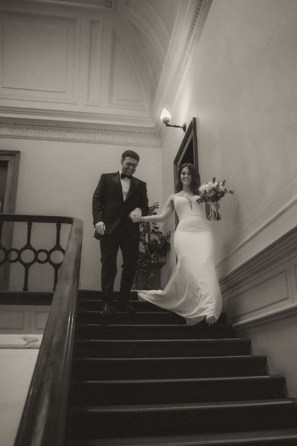 A series of black and white photos showing a couple descending a grand staircase in formal wedding attire.