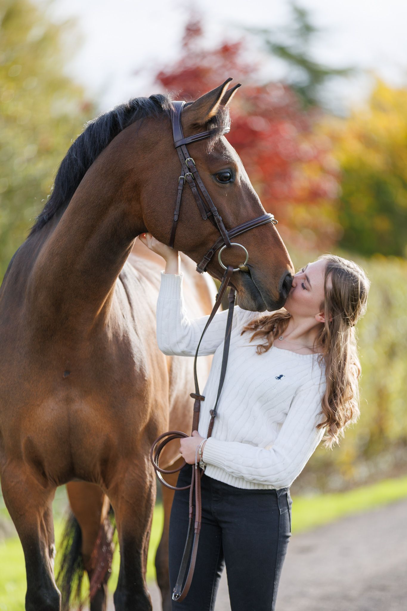 A person in a flowing red gown poses with a majestic black horse in an autumn forest setting.