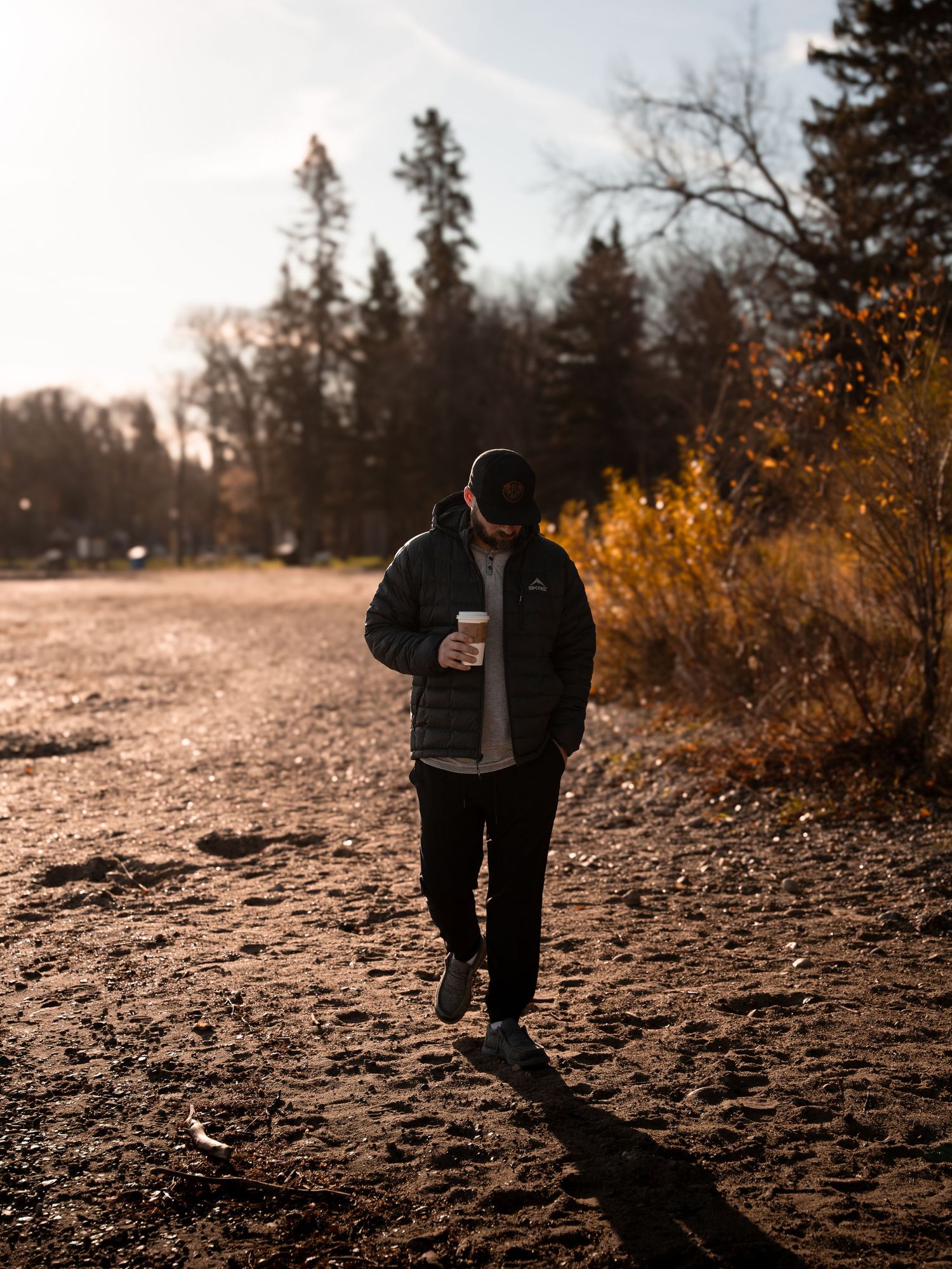 Silhouetted figure walks along dirt path during golden hour with coffee cup in hand.