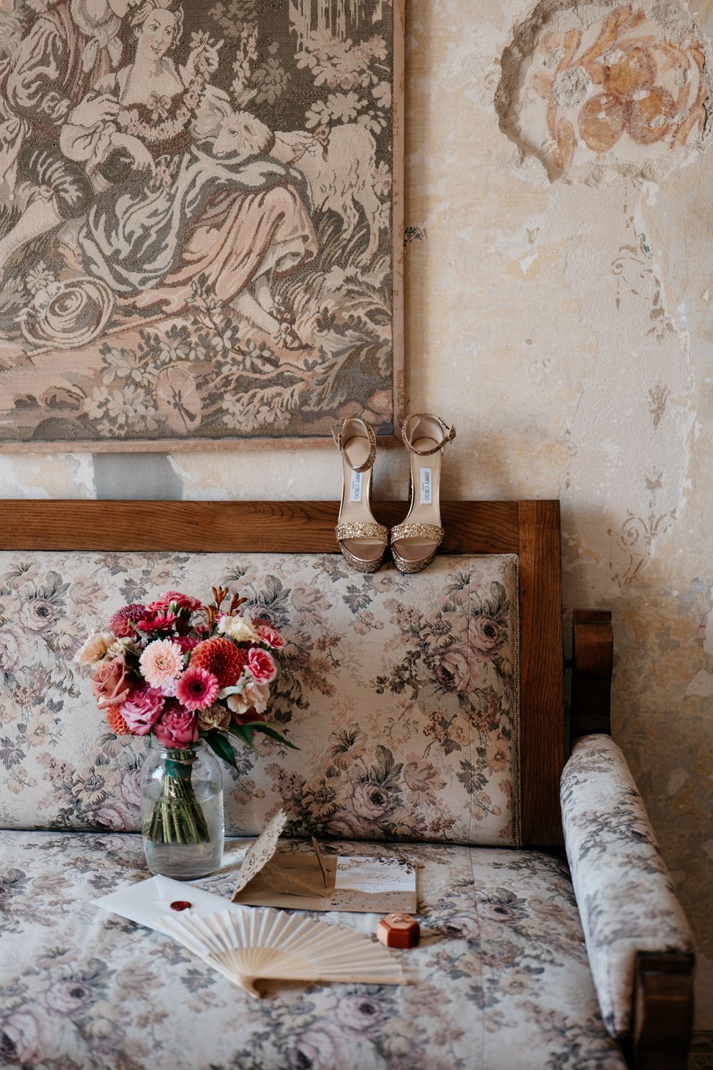 A romantic vintage setting with floral wallpaper, pink roses in a vase, and a decorative paper fan on a couch.