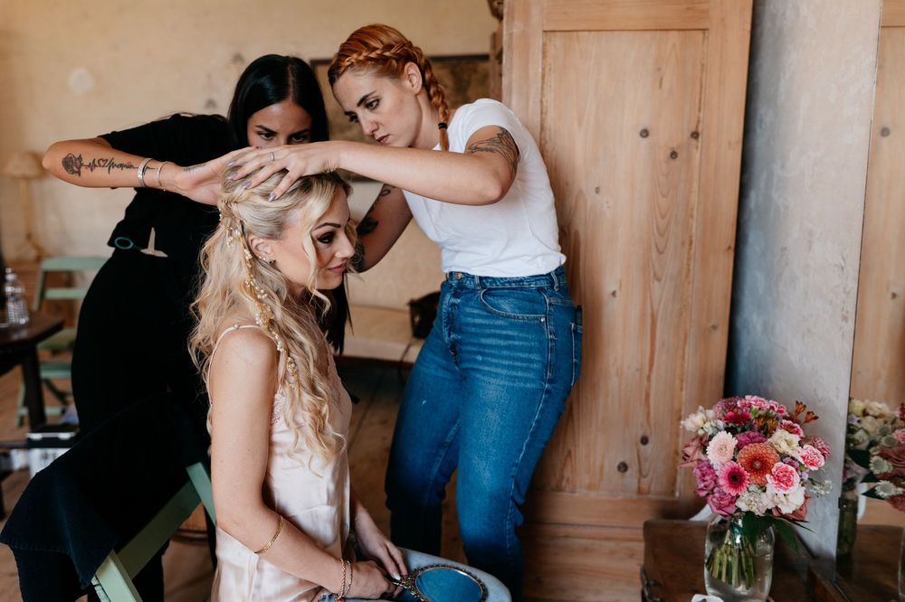 People getting ready in a rustic wooden room with flowers and natural light streaming through windows.