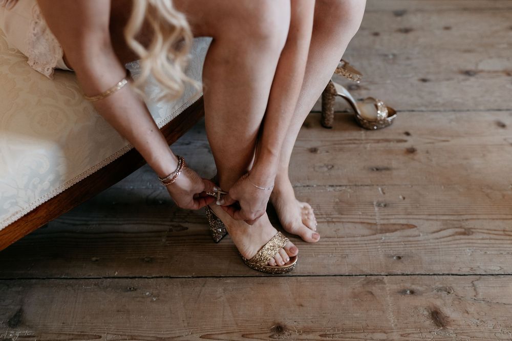 Close-up view of hands fastening straps on wedding sandals on wooden floor.