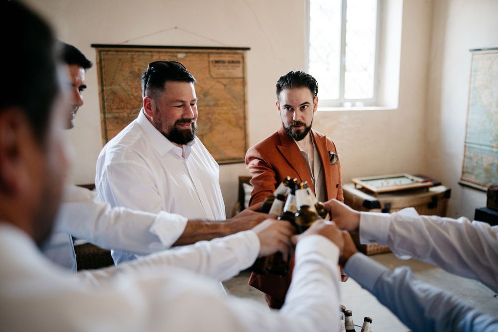 Groomsmen toasting with drinks during wedding preparations in bright room.