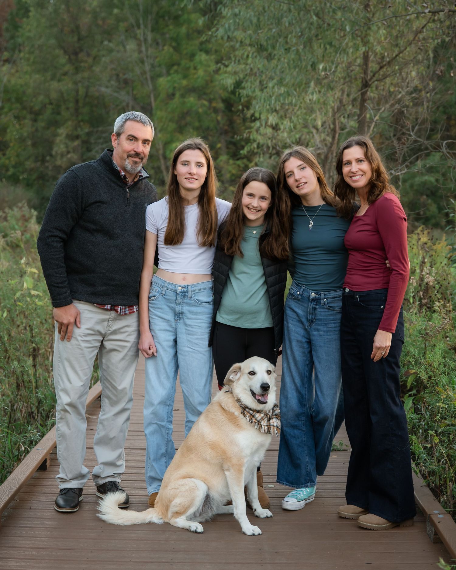 A group poses together on a wooden boardwalk with their friendly golden retriever dog in an outdoor nature setting.
