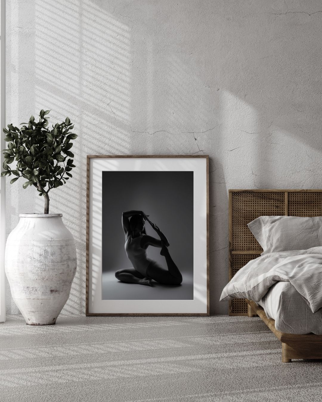 Minimalist bedroom interior with black and white artwork, white vase with plant, and natural rattan bed frame.