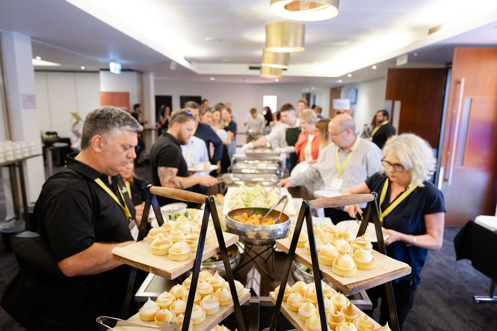 Photos of attendees lining up at a buffet with silver serving trays. Fremantle Conference Photographer