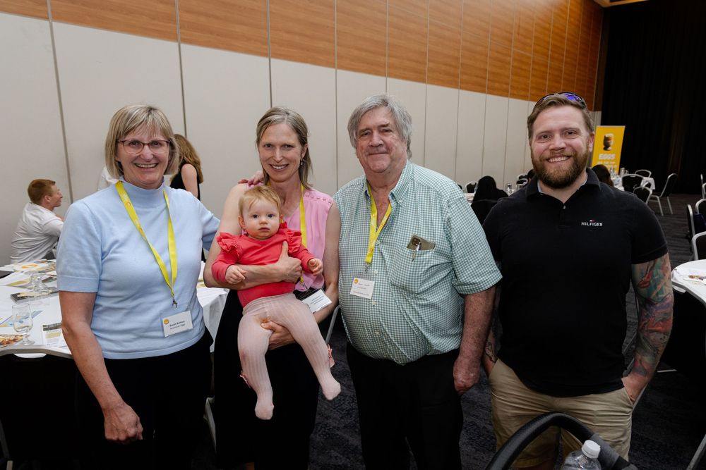 A group of people wearing event badges gather together at an indoor venue, photography by Kirsten Graham