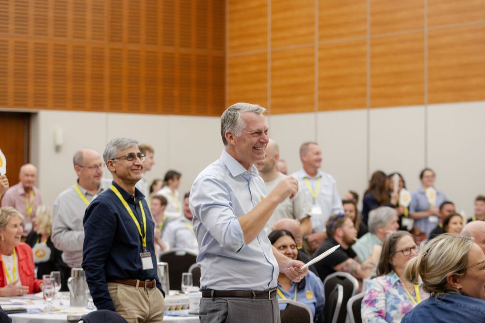 Conference attendees seated at round tables in a large meeting room during a professional event. Fremantle Conference Photography