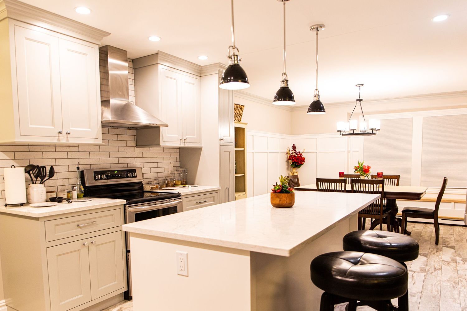 A modern white kitchen with pendant lights, quartz countertops, and hardwood floors features a large center island.