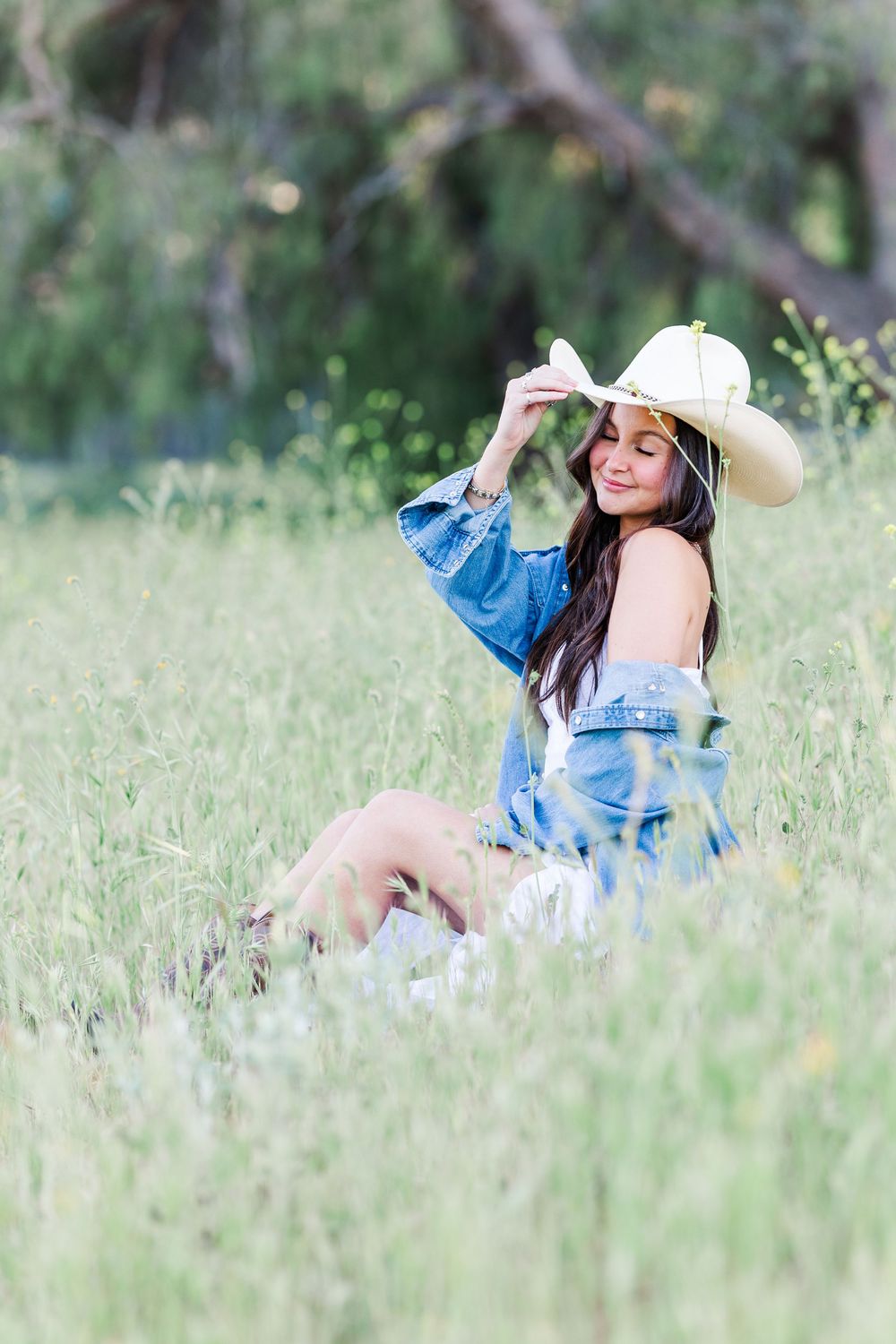 A person in a denim jacket and sun hat lies in a grassy meadow on a sunny day.