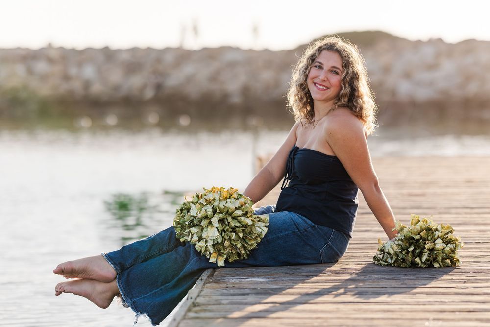 A woman in a navy blue dress sits gracefully on wooden steps holding a bouquet of white flowers at sunset.
