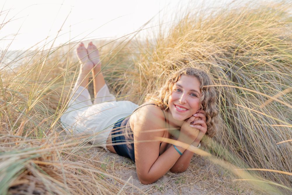 Relaxed person lying in tall beach grass at sunset wearing a white dress.