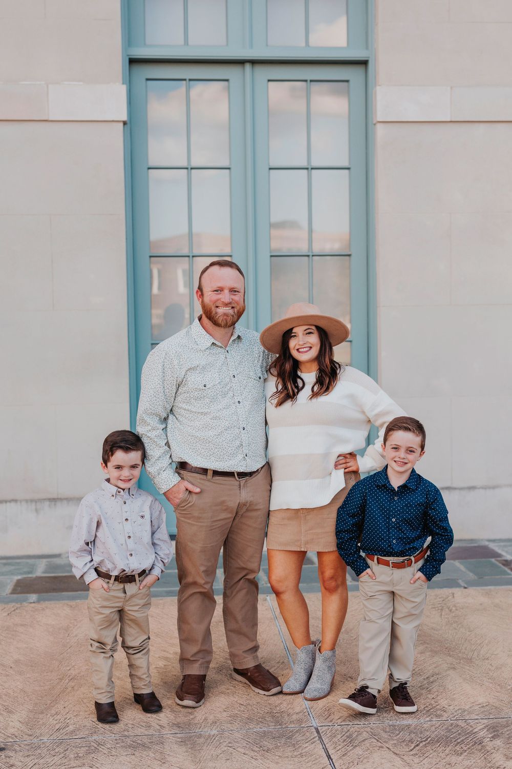 Family of four poses together in casual attire against blue door and beige wall.