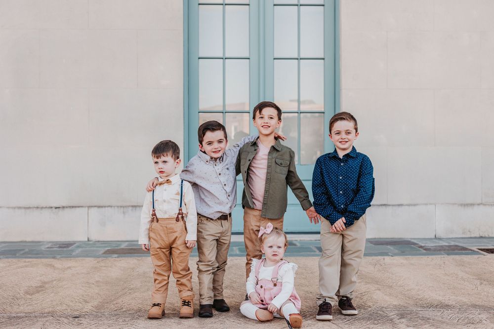 Group of children pose together in coordinated outfits against neutral building exterior.