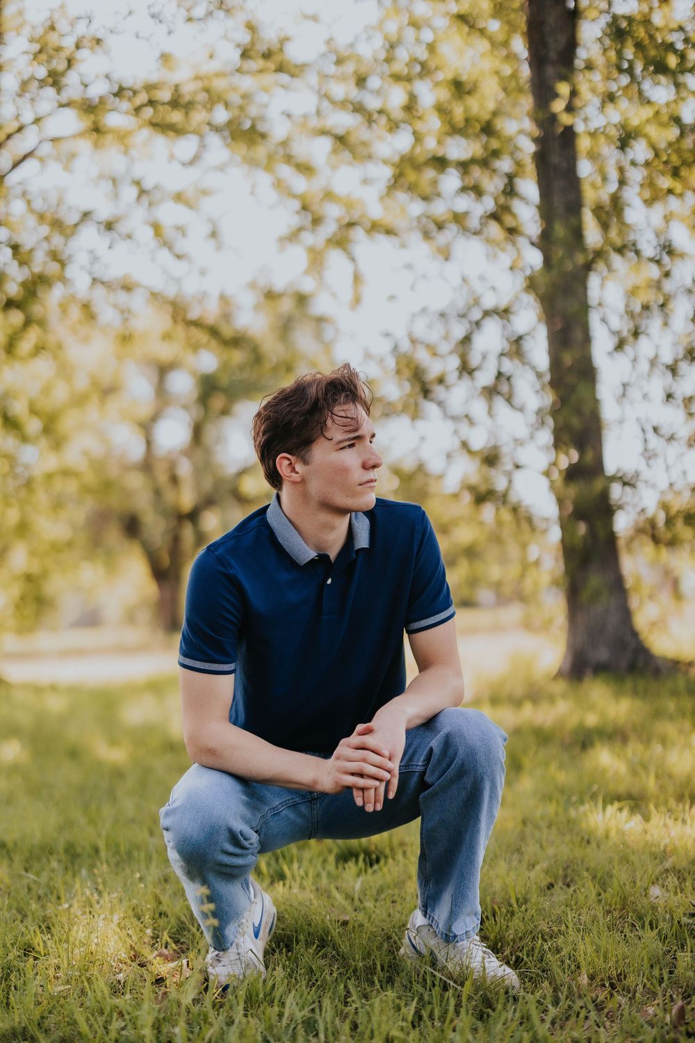 Person in casual attire crouching on grassy hill during golden hour.