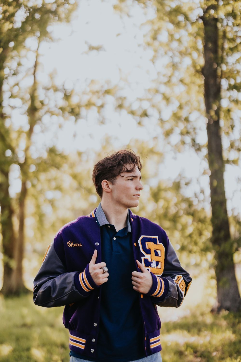 Person in navy varsity jacket making gestures against autumn trees in golden light.