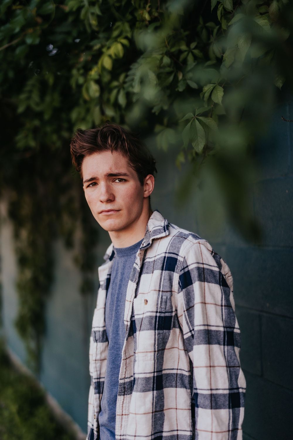 Person wearing plaid flannel shirt poses against leafy green background.