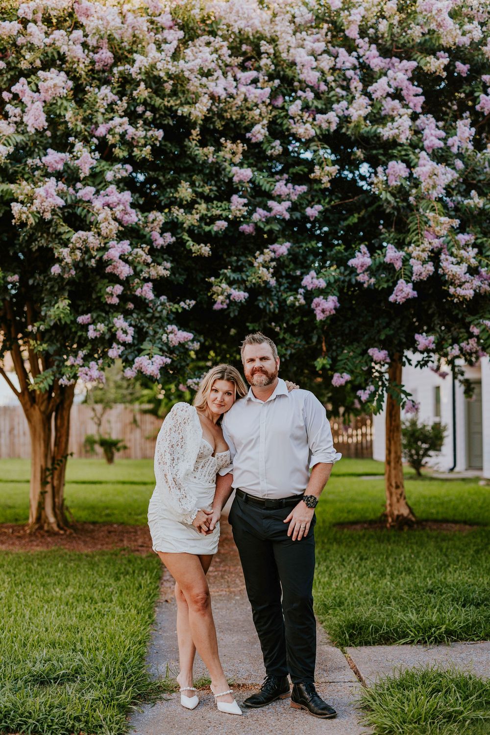 Couple posing under blooming pink cherry blossom trees in park setting.