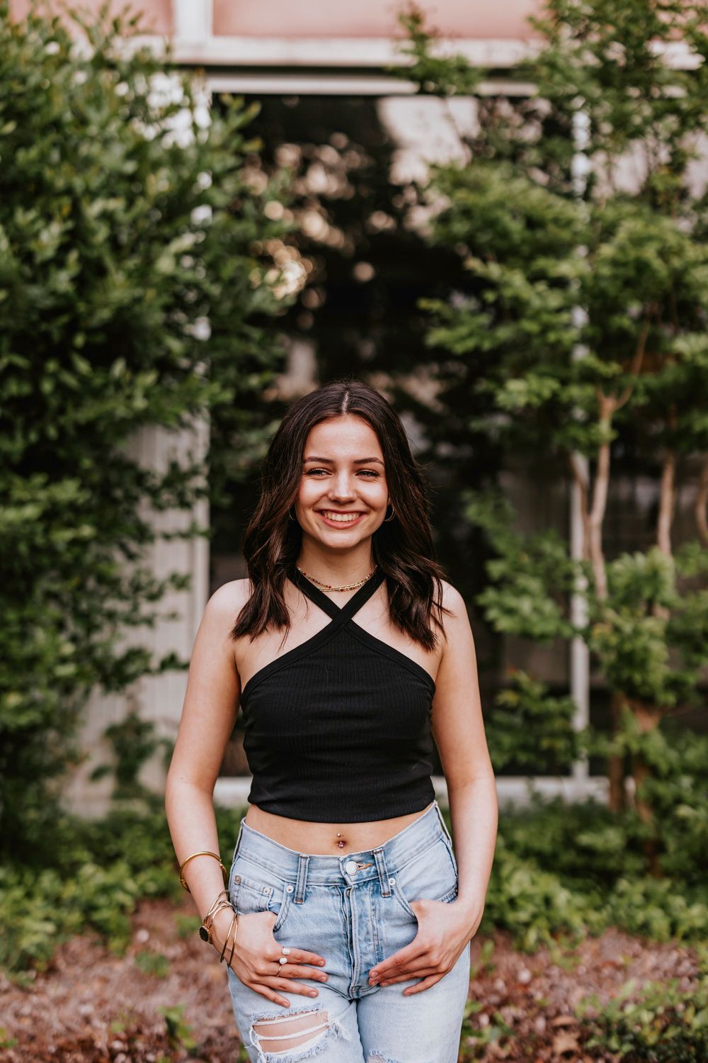Casual outdoor portrait in black crop top and denim jeans among greenery.