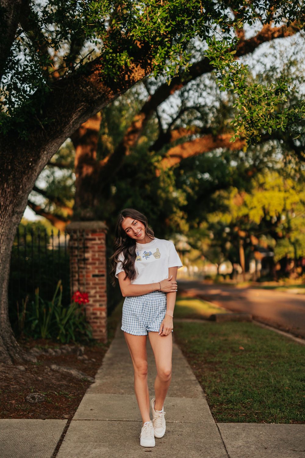 Person walking on a sidewalk wearing white sneakers and shorts in a sunny outdoor setting.