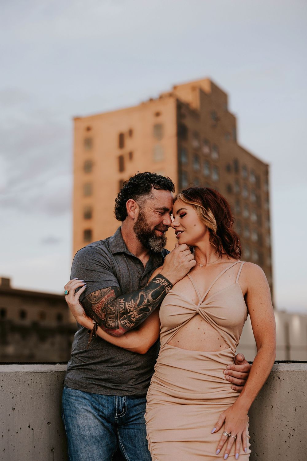 Intimate couple sharing tender moments during sunset photoshoot with city buildings in background.