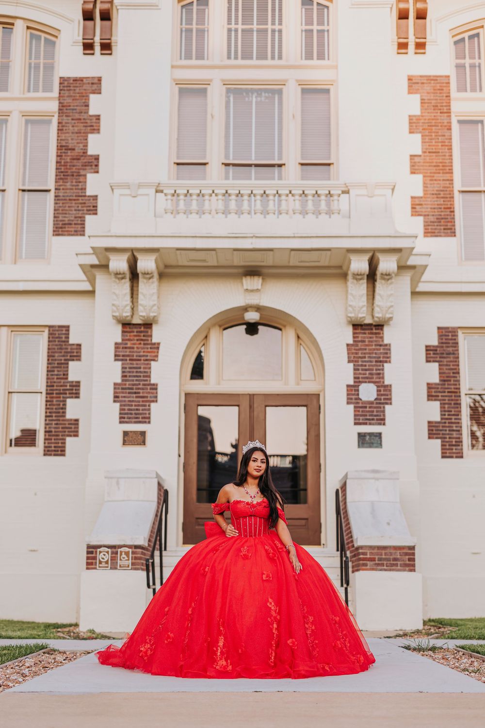 A stunning red ballgown dress photographed against a classic architectural backdrop with white columns and brick details.