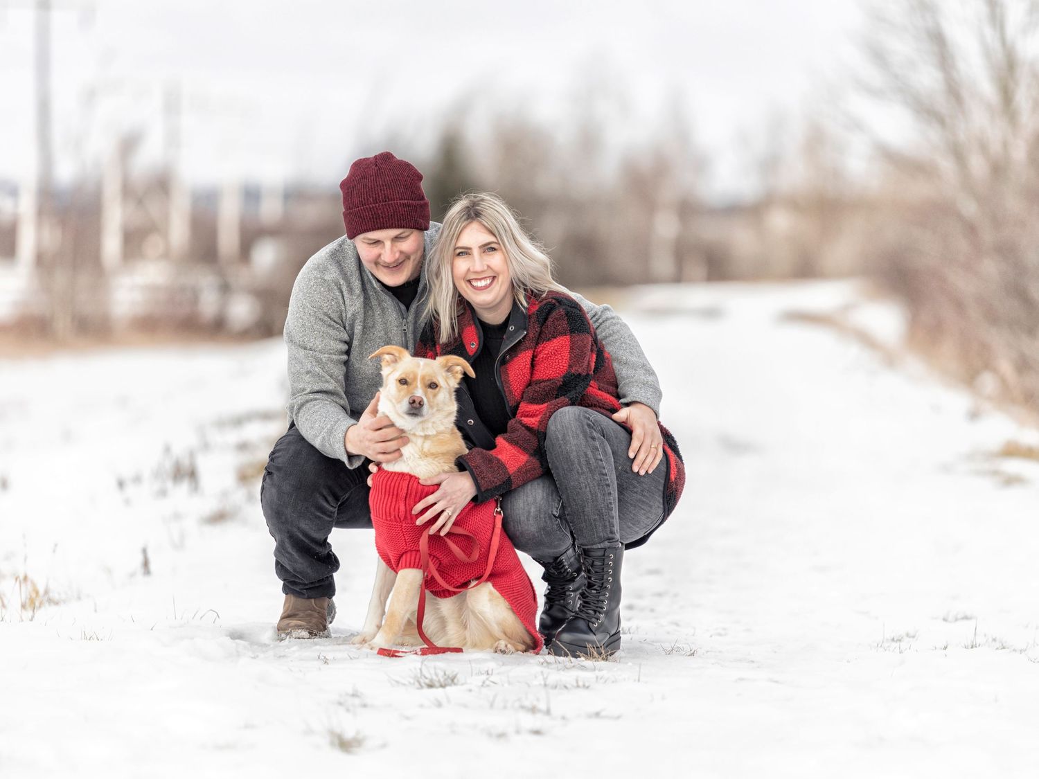 Couple and small dog pose together in winter snow scene during outdoor photo session.