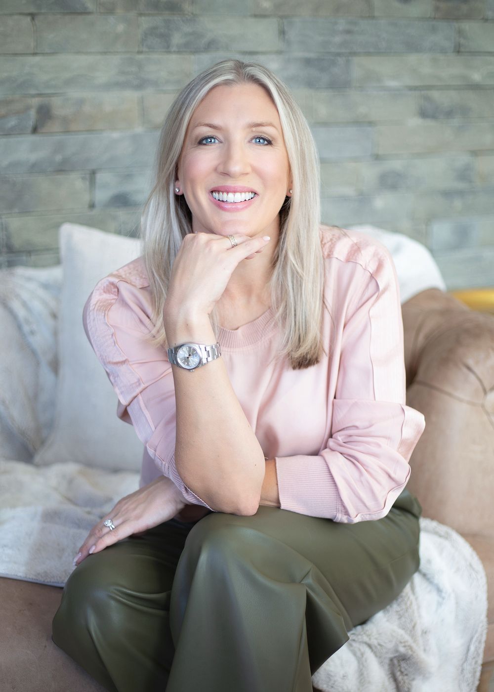 A person wearing a pink sweater and olive pants sits casually on a couch in a modern living room setting.
