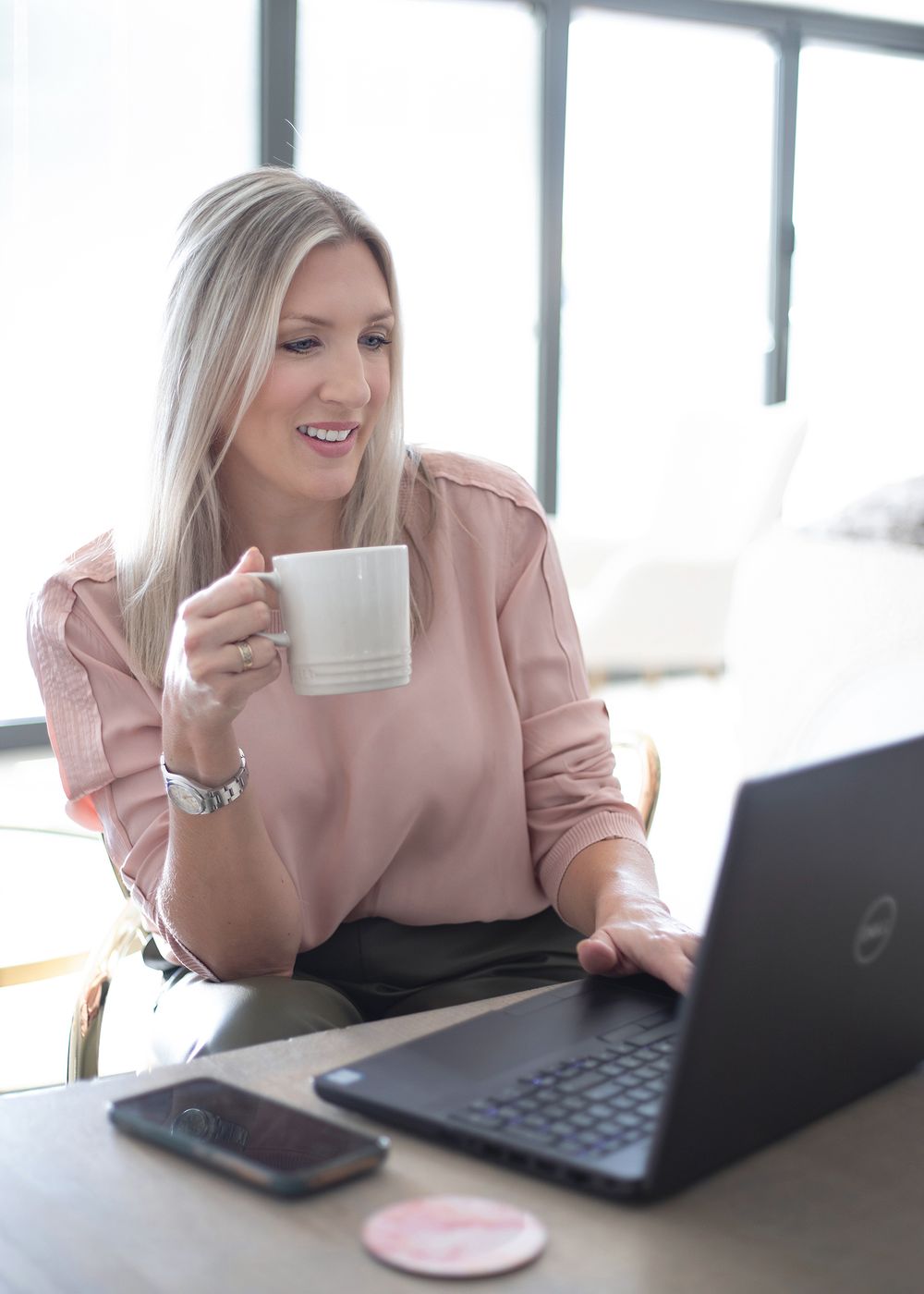 Professional working at desk with laptop and coffee cup in bright modern office space.
