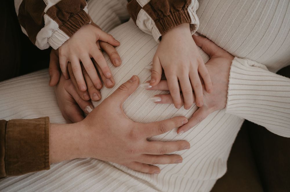 Family hands layered together on a pregnant woman's belly, symbolizing love and anticipation of new life.
