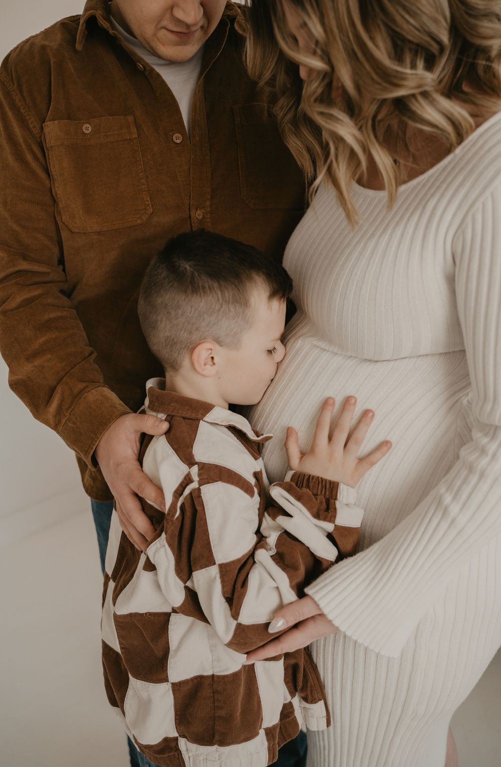 A young boy kisses his mothers pregnant belly during a maternity photo session.