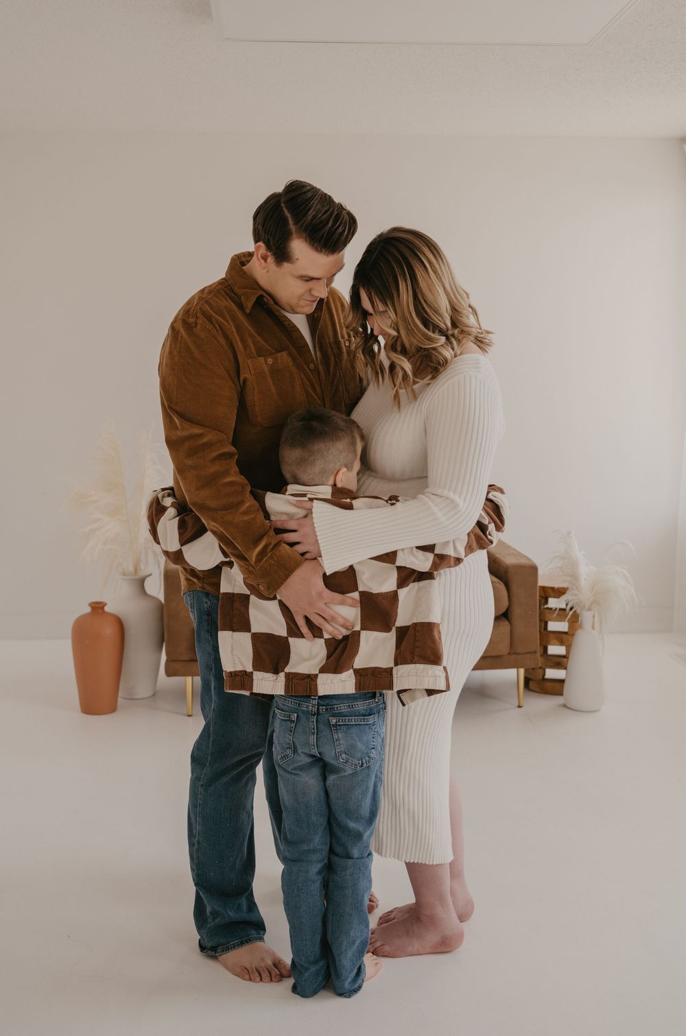 A loving family of three shares a tender embrace during a maternity photo session.