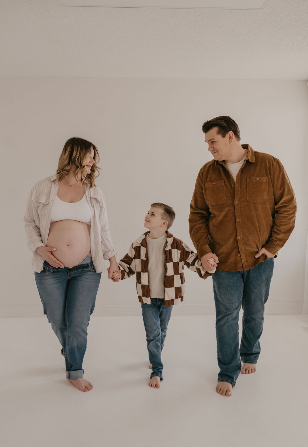 Expecting parents walk hand-in-hand with their young son during a maternity photo session.