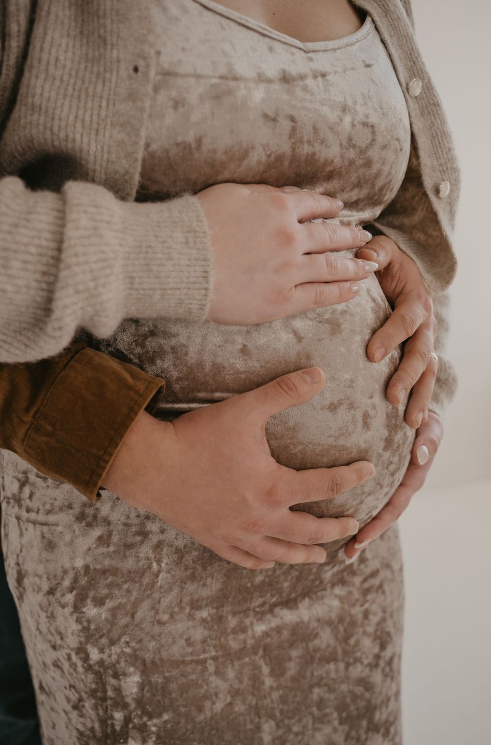 Close-up of couple's hands cradling pregnant belly in velvet maternity outfit during photoshoot.