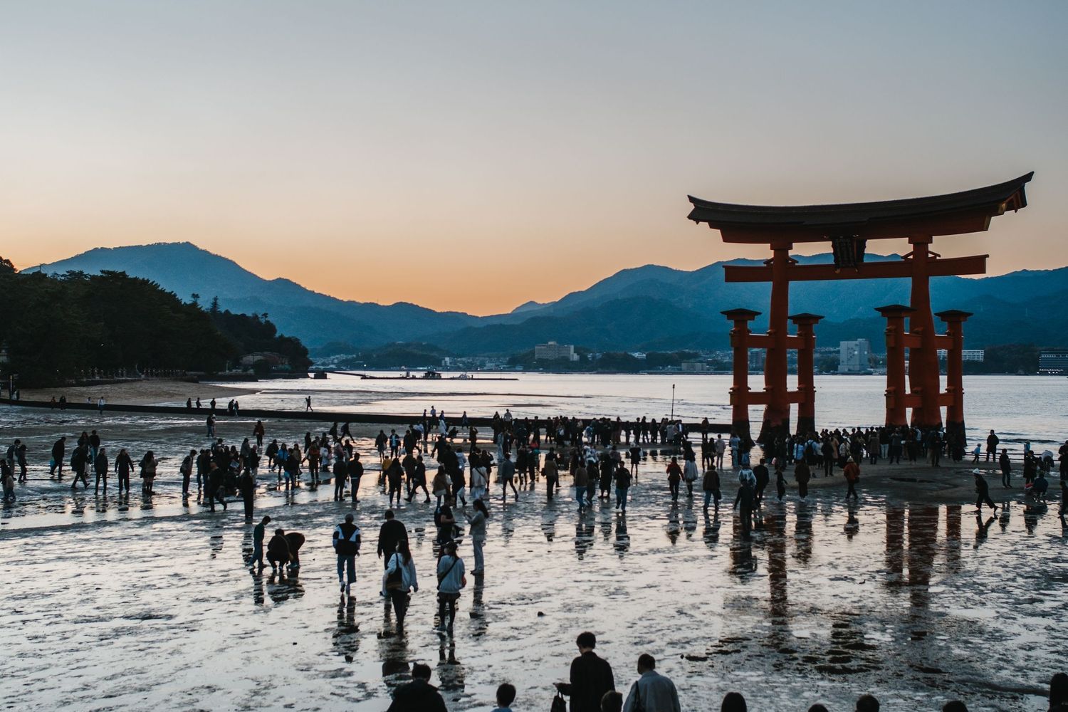 Silhouettes of visitors explore the iconic Itsukushima Shrine floating torii gate at sunset in Miyajima, Japan.