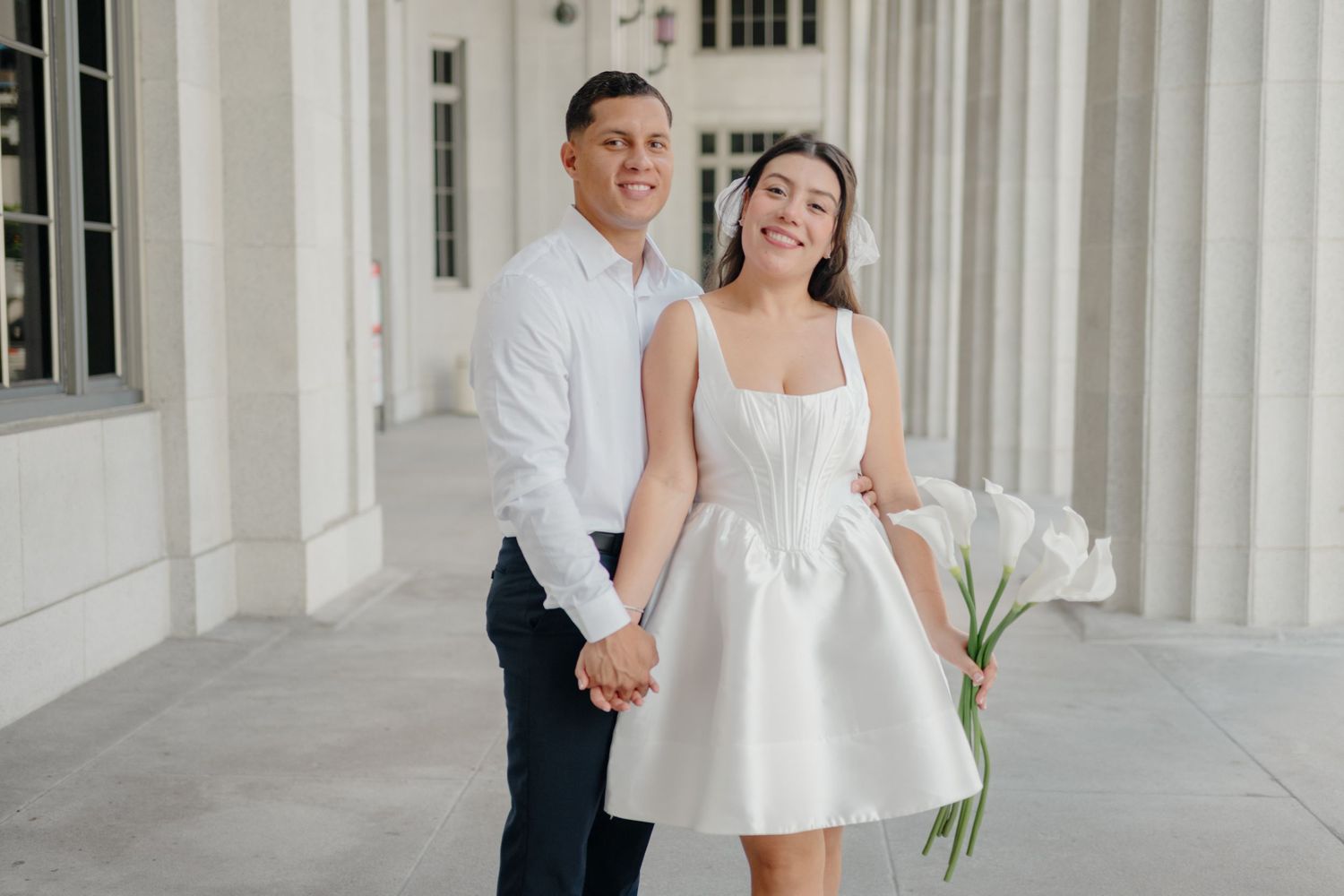 A couple shares a joyful moment together in a white dress and formal attire among elegant white columns.