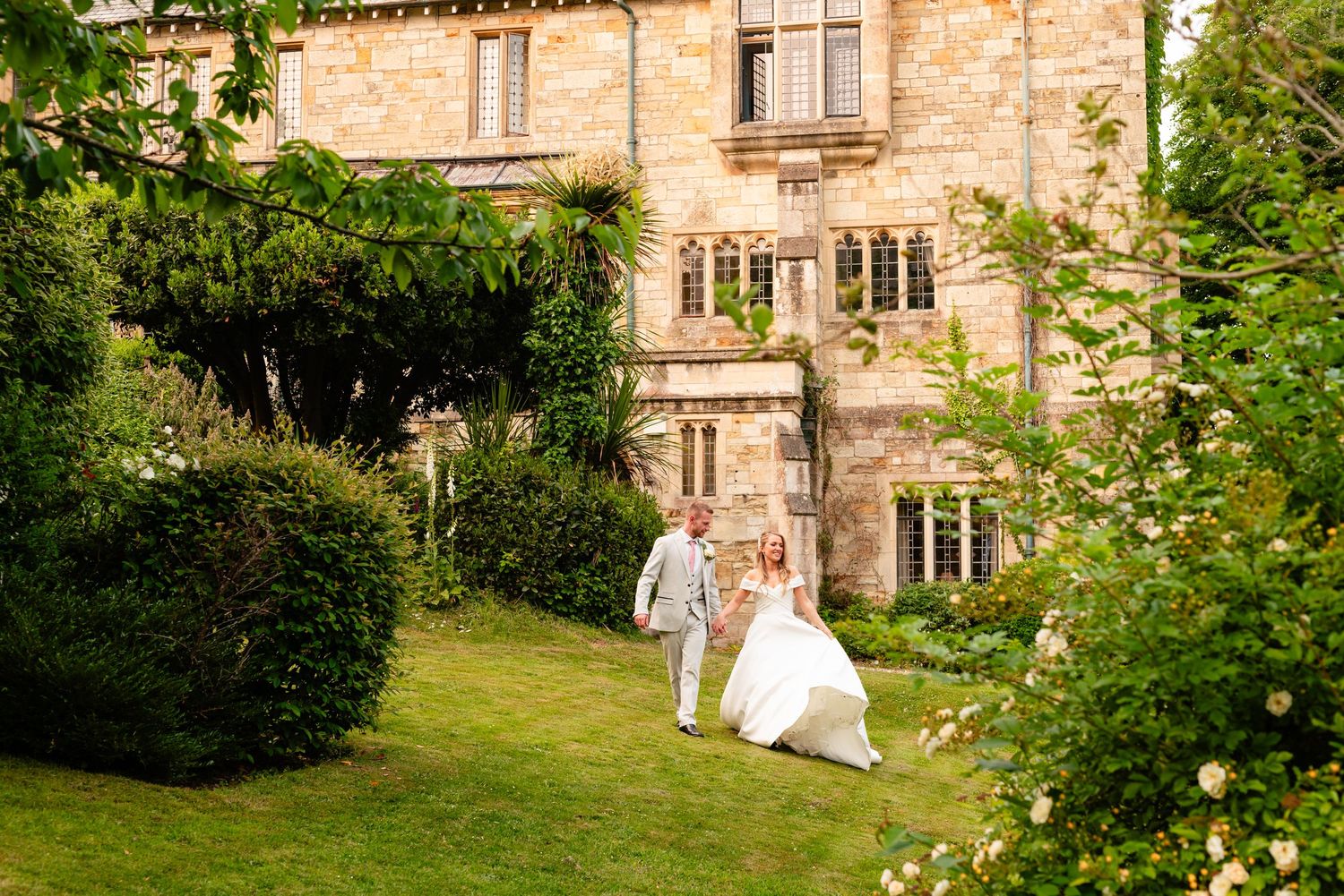 Decorative image. Bride and groom walking across the lawn at the Alverton Hotel, Truro, surrounded by the gardens and flowers.