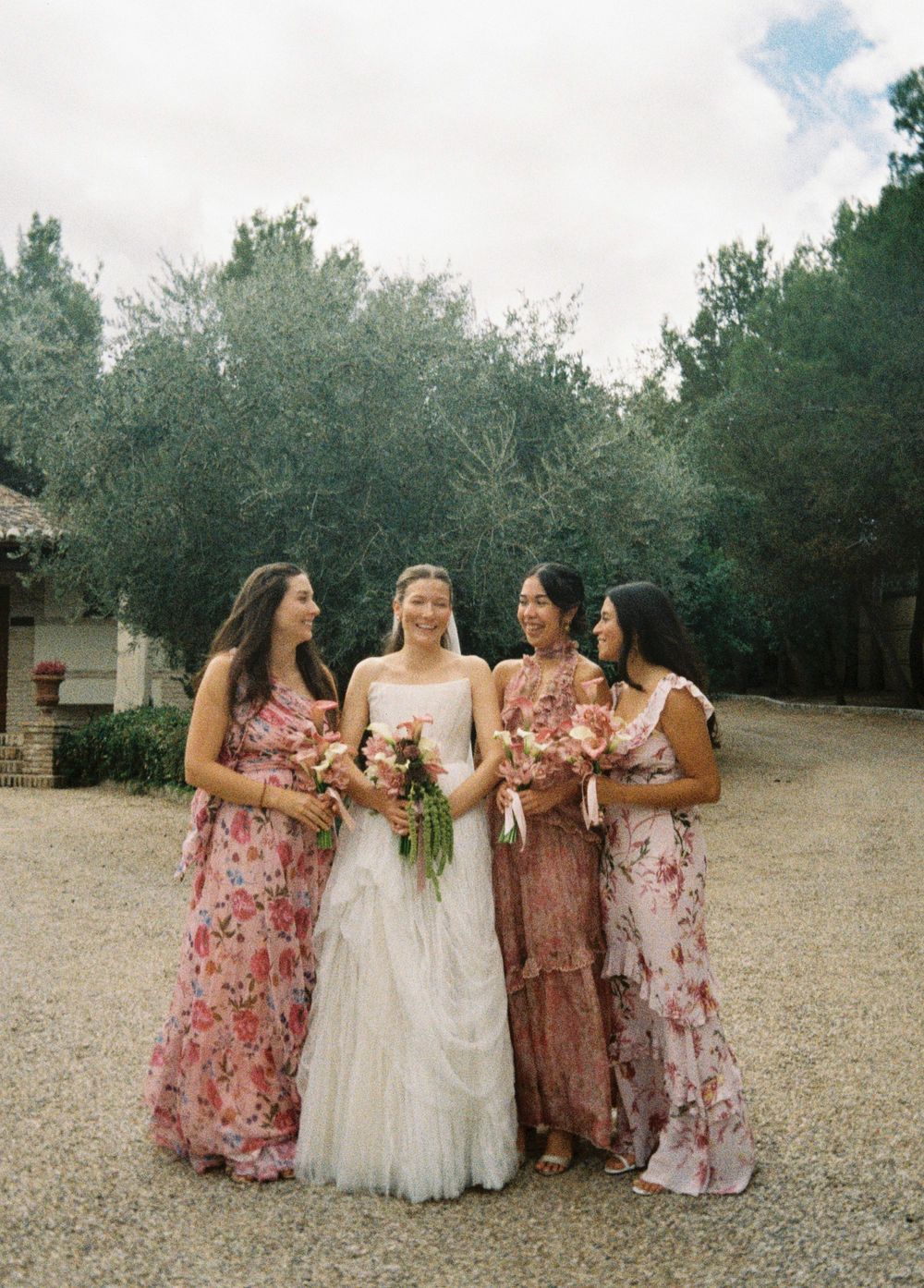 A wedding party in floral dresses walks together across a rustic outdoor setting.