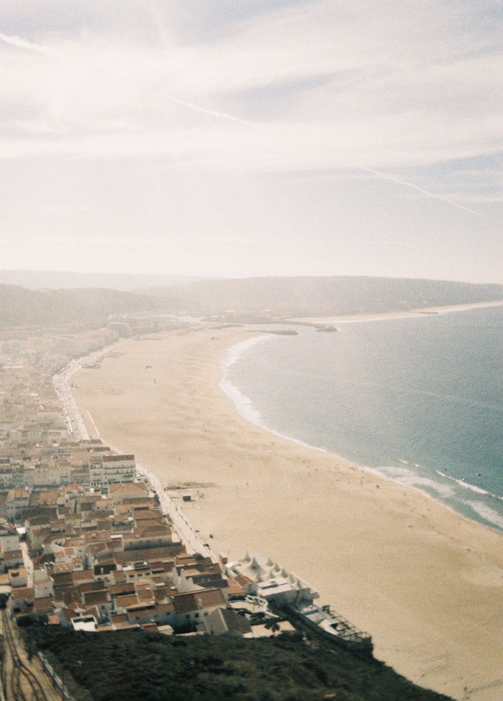 Aerial panoramic view of a long sandy beach coastline with urban development and ocean waves stretching into the distance.