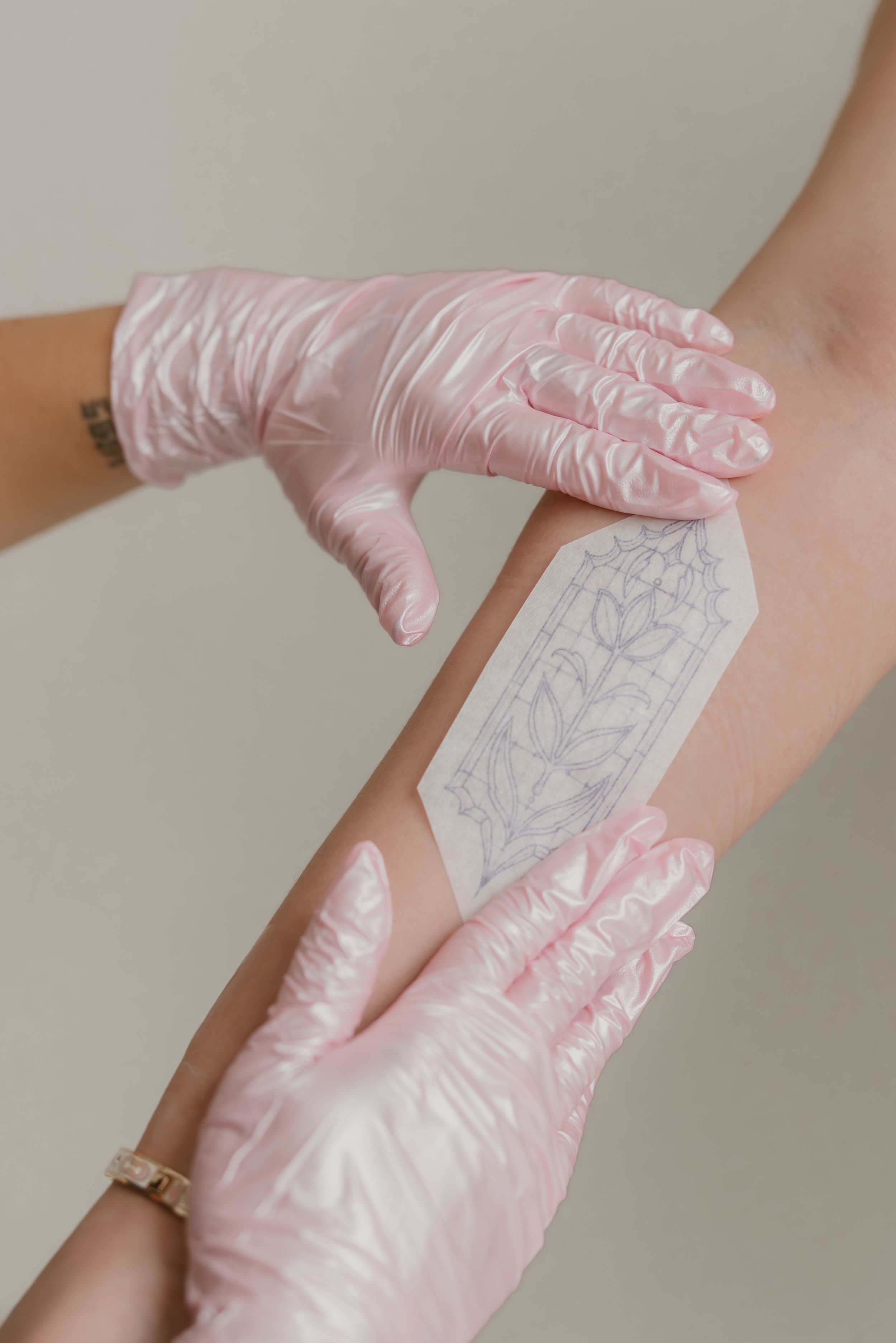 Process showing the application of a temporary tattoo design transfer onto skin with gloved hands.